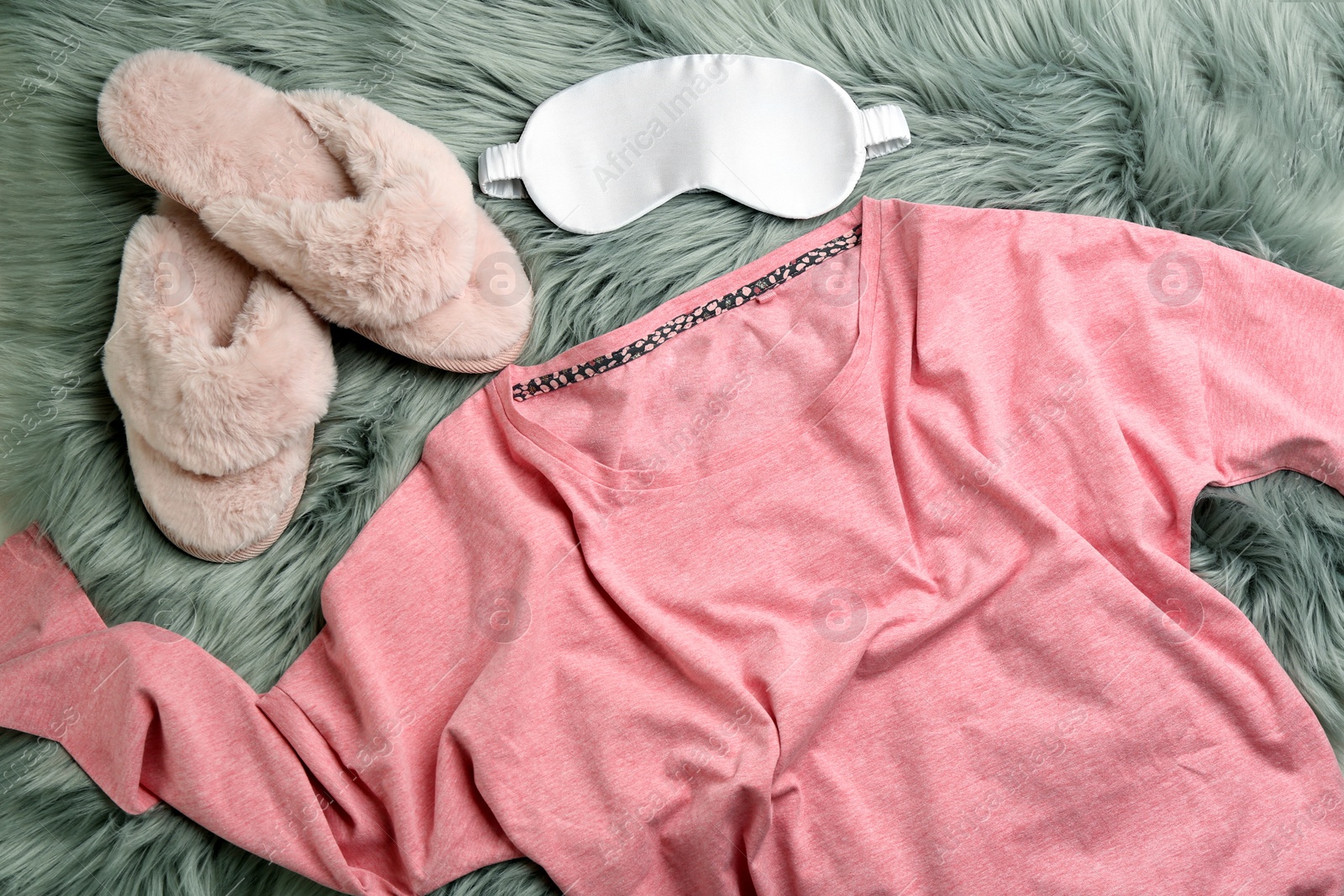 Photo of Pair of fluffy slippers, pajamas and sleeping eye mask on fuzzy carpet, flat lay. Comfortable home outfit