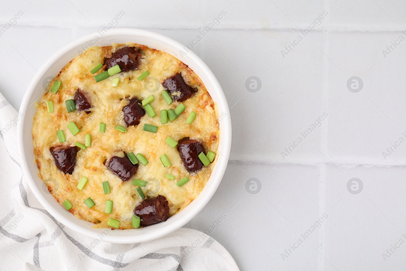 Photo of Tasty sausage casserole with green onions in baking dish on white tiled table, top view. Space for text