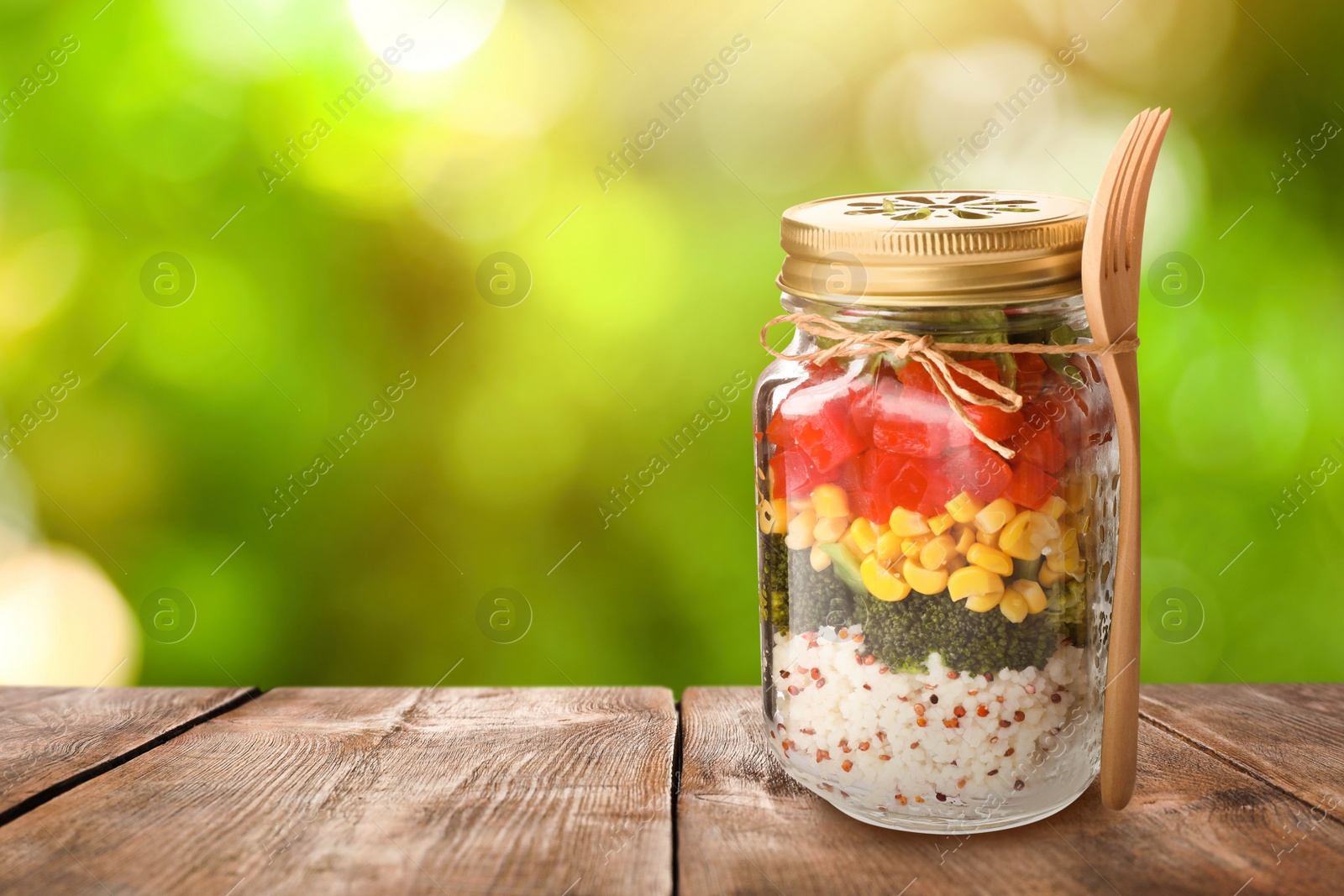 Image of Jar with healthy meal and fork on wooden table against blurred background, space for text