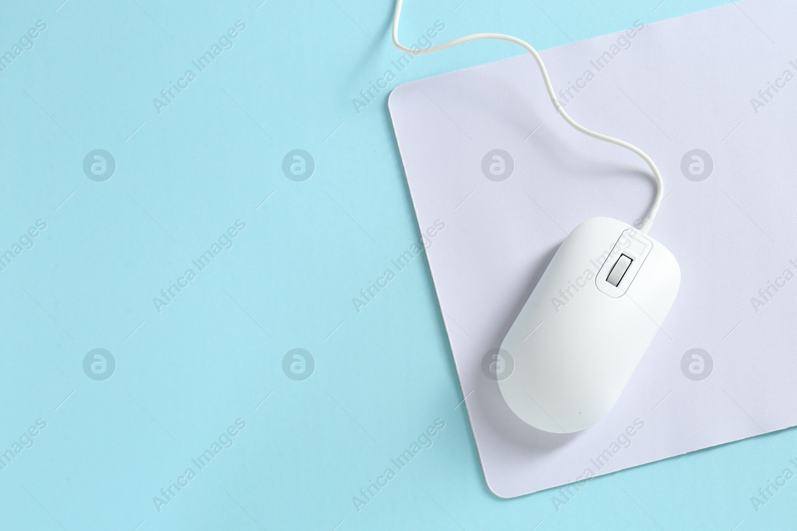 Photo of Wired mouse and mousepad on light blue background, top view. Space for text