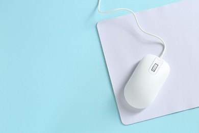 Photo of Wired mouse and mousepad on light blue background, top view. Space for text