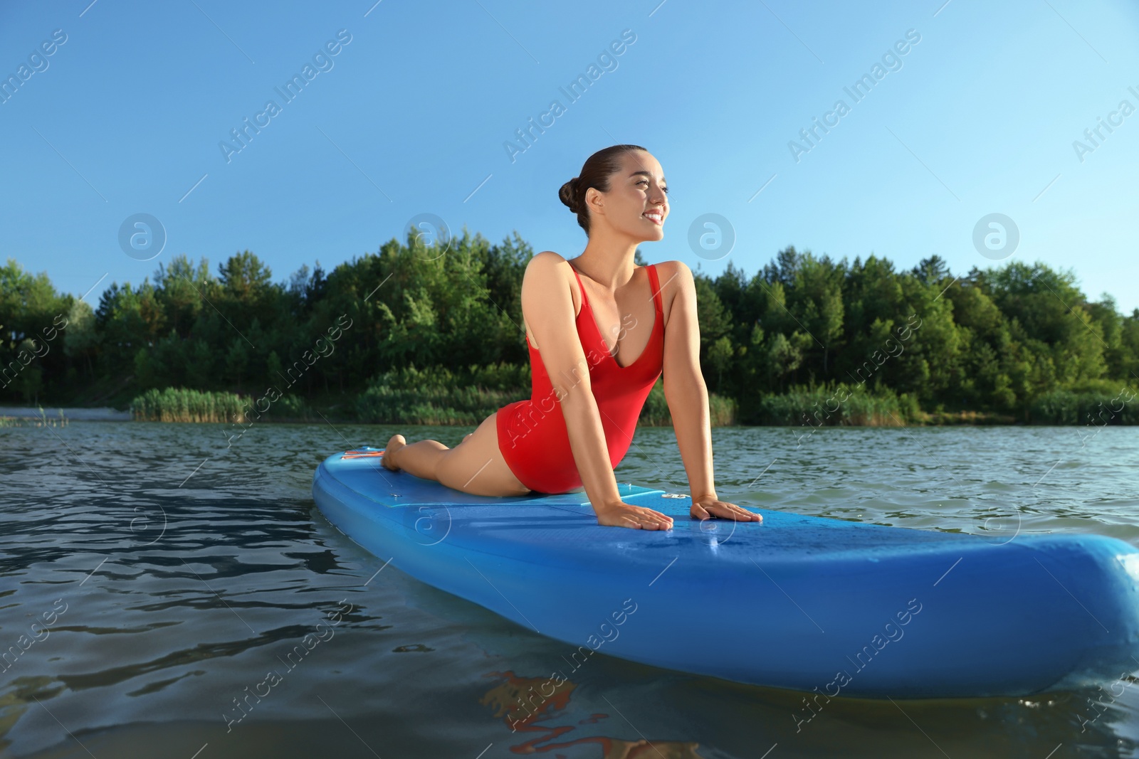 Photo of Young woman practicing yoga on light blue SUP board on river