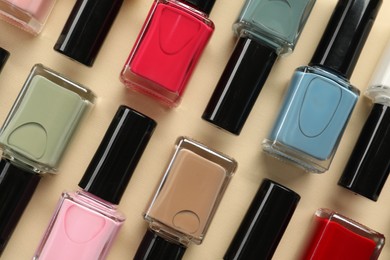 Bright nail polishes in bottles on beige background, flat lay