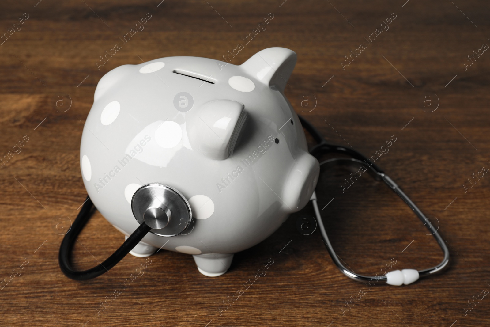 Photo of Light gray ceramic piggy bank and stethoscope on wooden table. Medical insurance