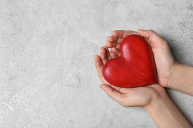 Woman holding heart on grey stone background, top view with space for text. Donation concept