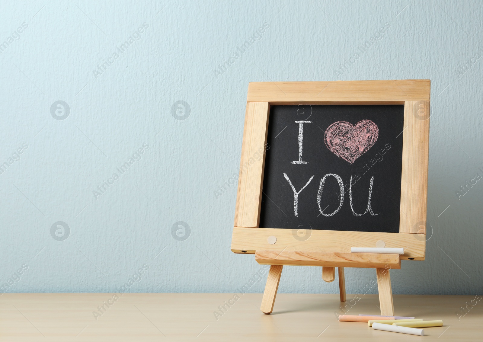 Photo of Chalkboard with words I LOVE YOU on table against blue background. Space for text