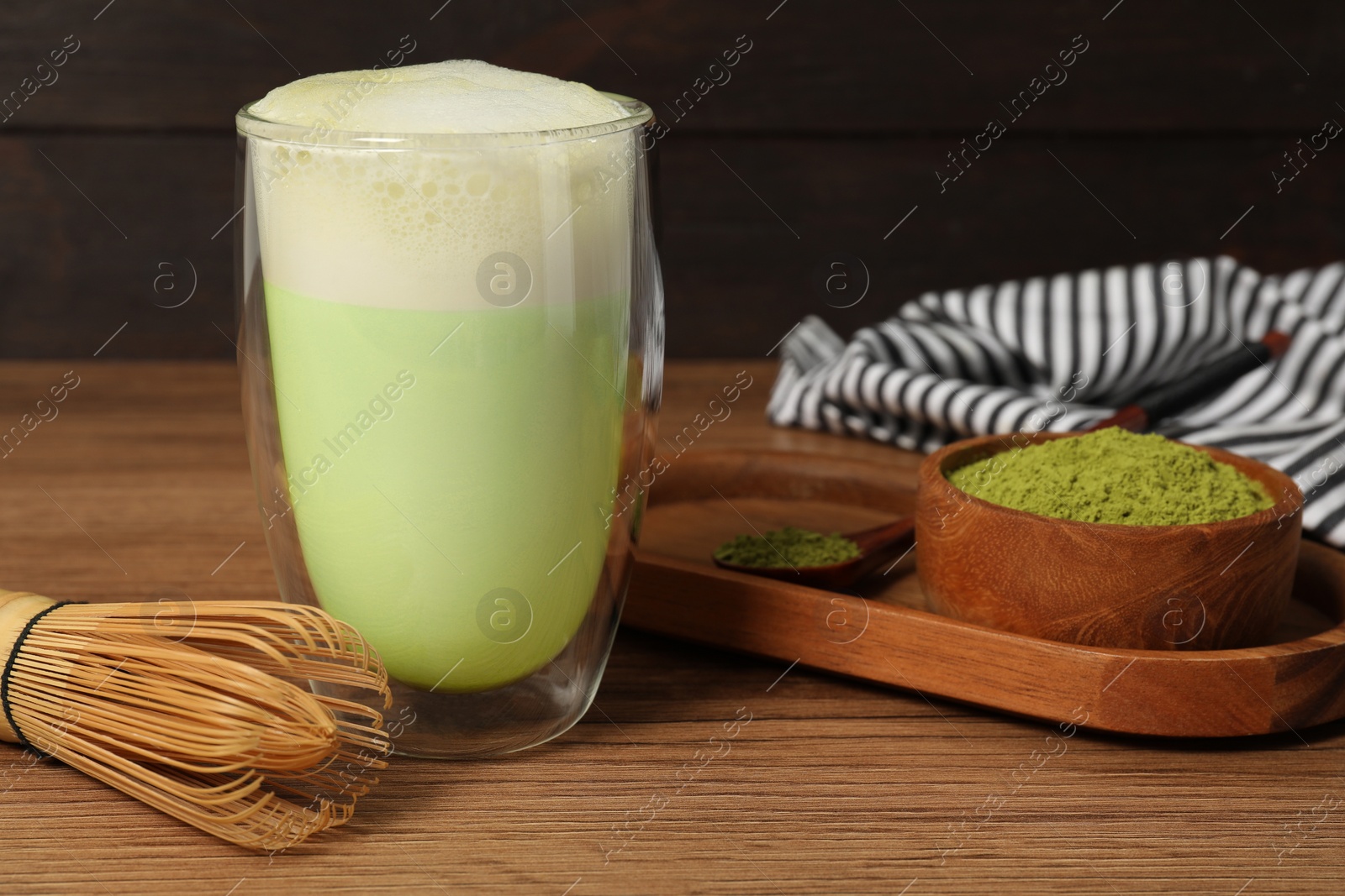 Photo of Glass of tasty matcha latte, bamboo whisk and green powder on wooden table, closeup