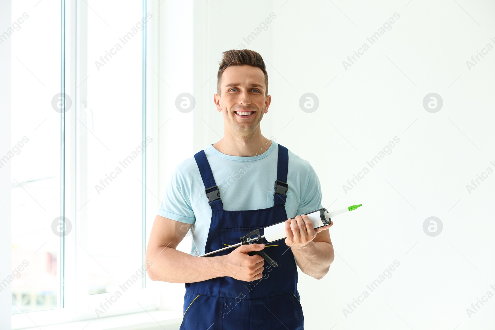 Photo of Construction worker in uniform with window sealant indoors