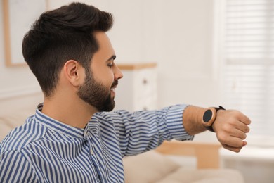 Photo of Young man looking at smart watch in apartment