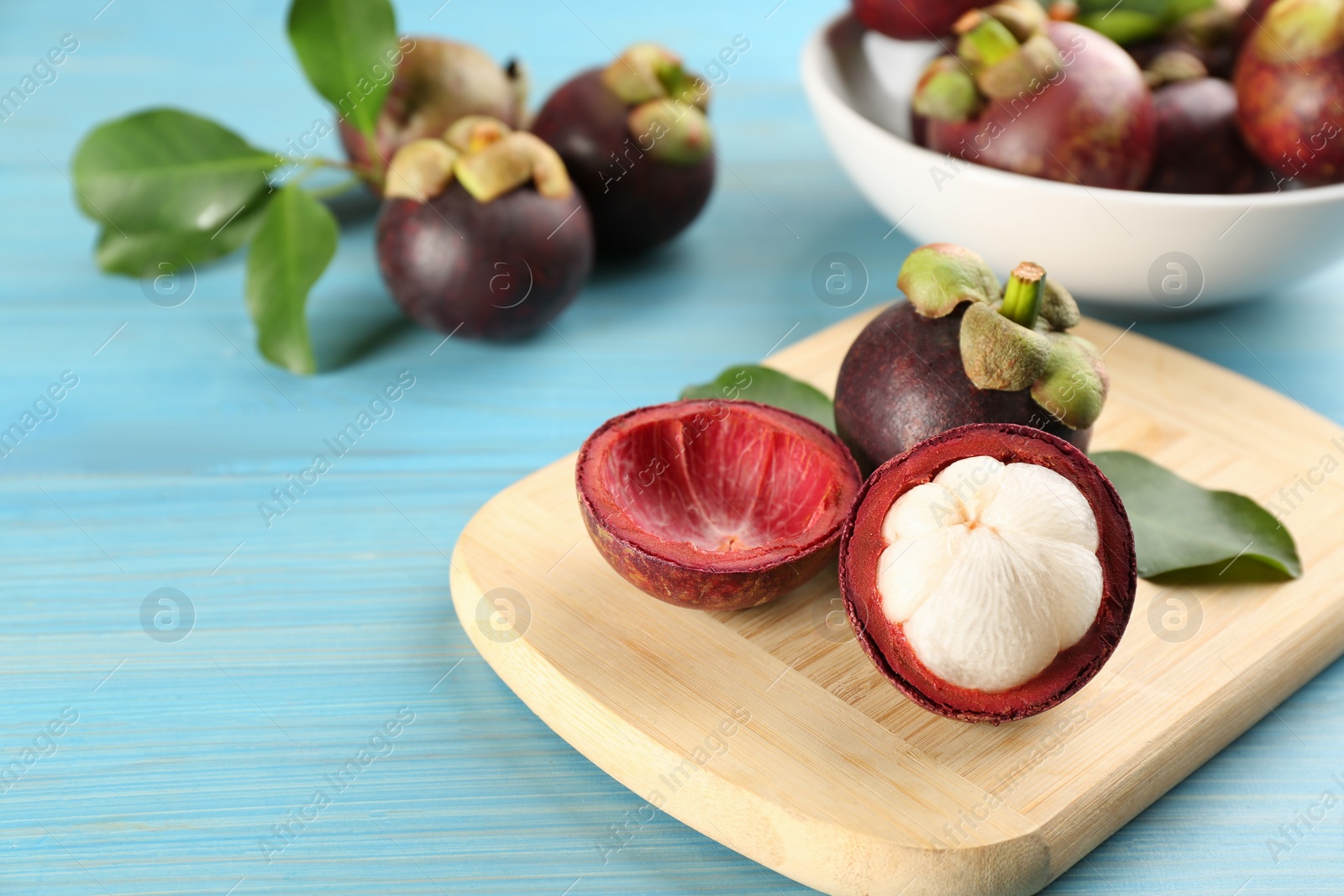 Photo of Fresh ripe mangosteen fruits on light blue wooden table. Space for text