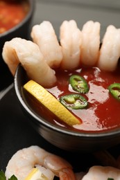 Photo of Tasty boiled shrimps with cocktail sauce, chili, parsley and lemon on table, closeup