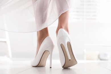 Photo of Young bride in beautiful wedding shoes walking indoors, back view