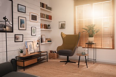 Cozy home library interior with comfortable armchair near window and collection of different books on shelves