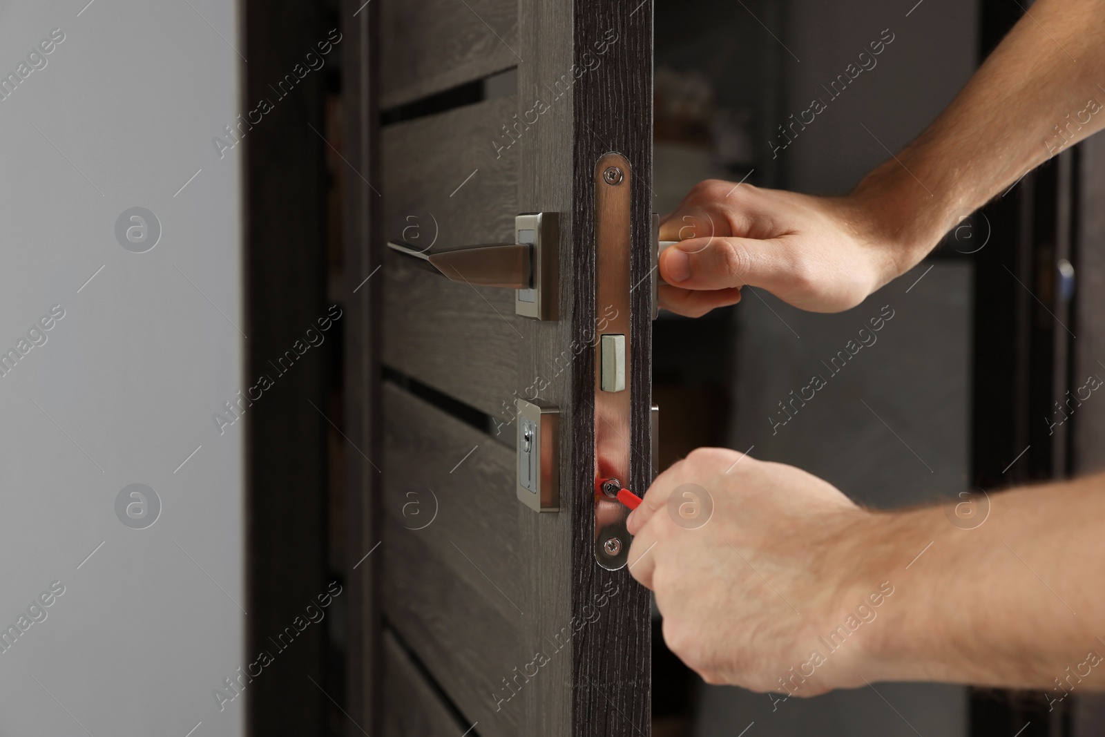 Photo of Worker with screwdriver repairing door lock indoors, closeup