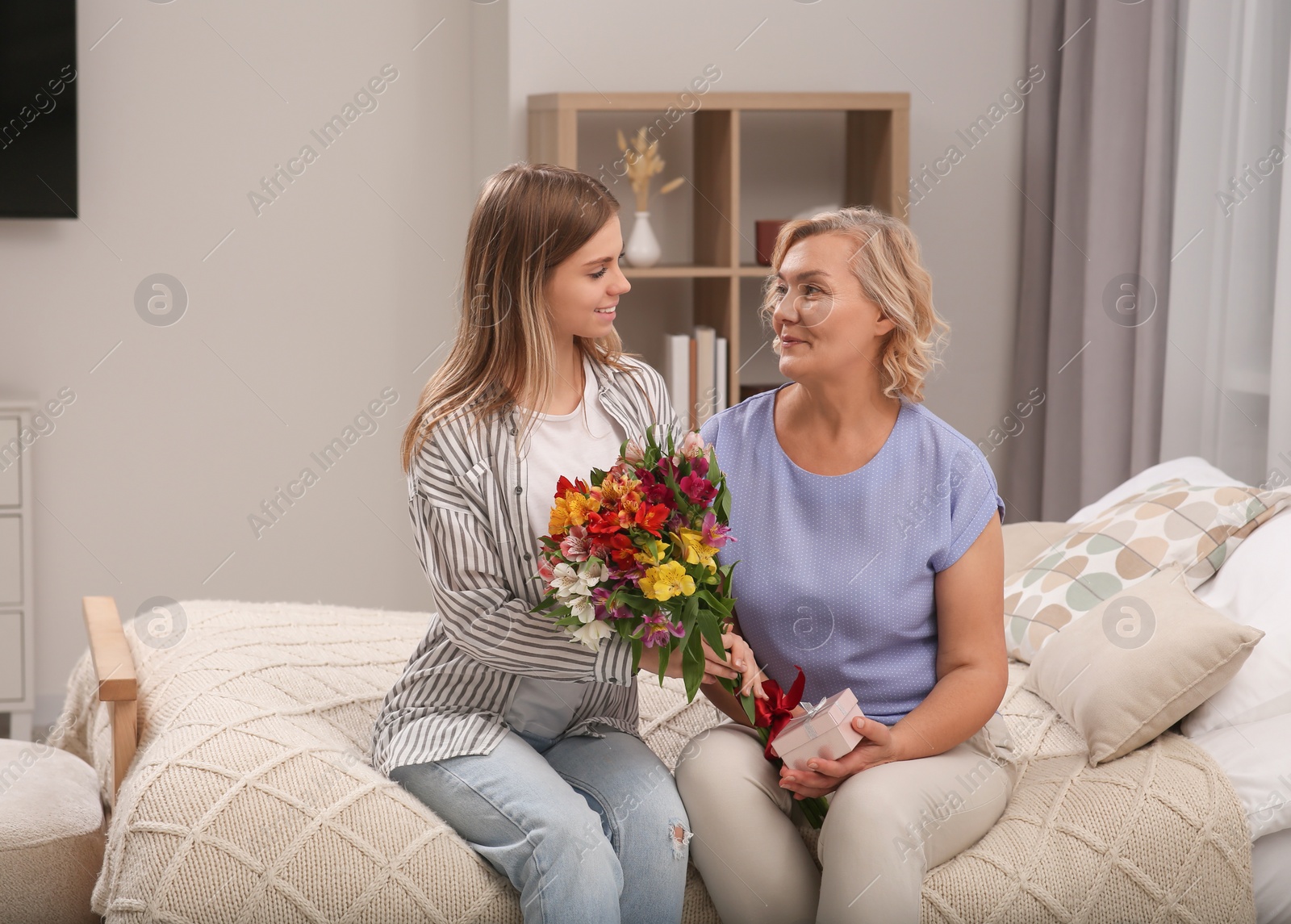 Photo of Young daughter congratulating her mom with flowers at home. Happy Mother's Day