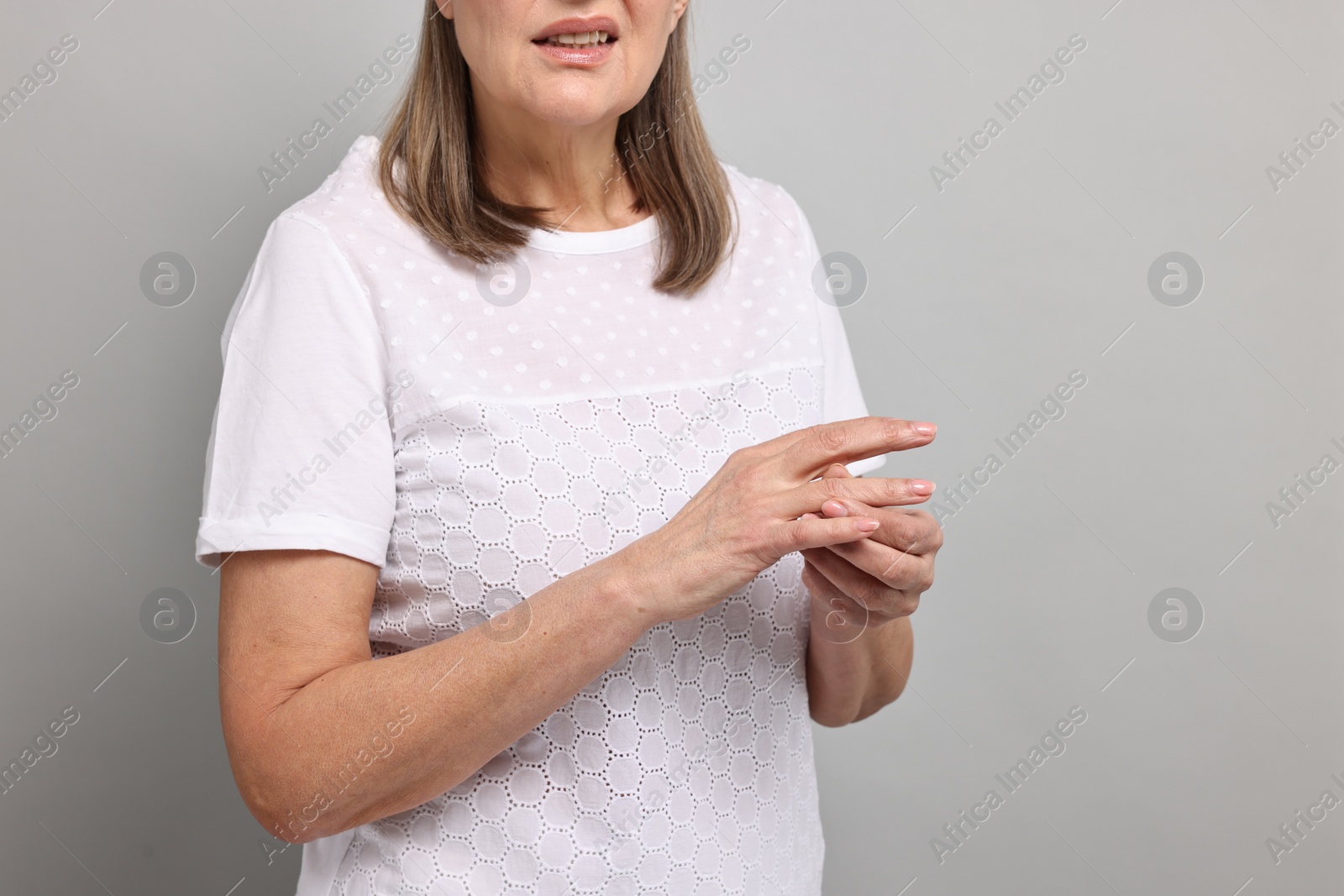 Photo of Arthritis symptoms. Woman suffering from pain in fingers on gray background, closeup