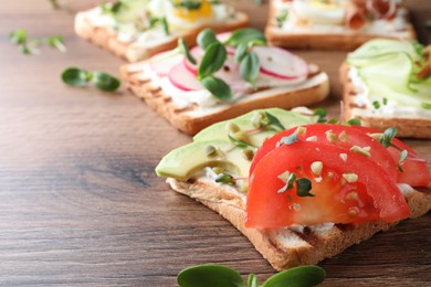 Photo of Different delicious sandwiches with microgreens on wooden table, closeup