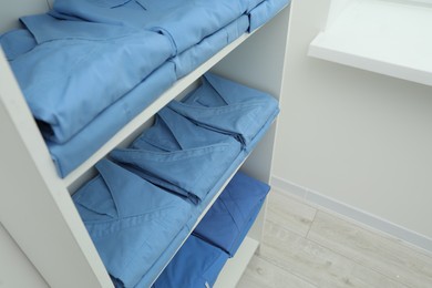 Light blue medical uniforms on white rack indoors, space for text