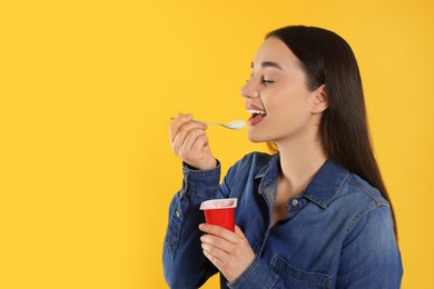 Photo of Happy woman eating tasty yogurt on orange background. Space for text