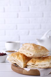 Delicious puff pastry on white wooden table against brick wall, space for text