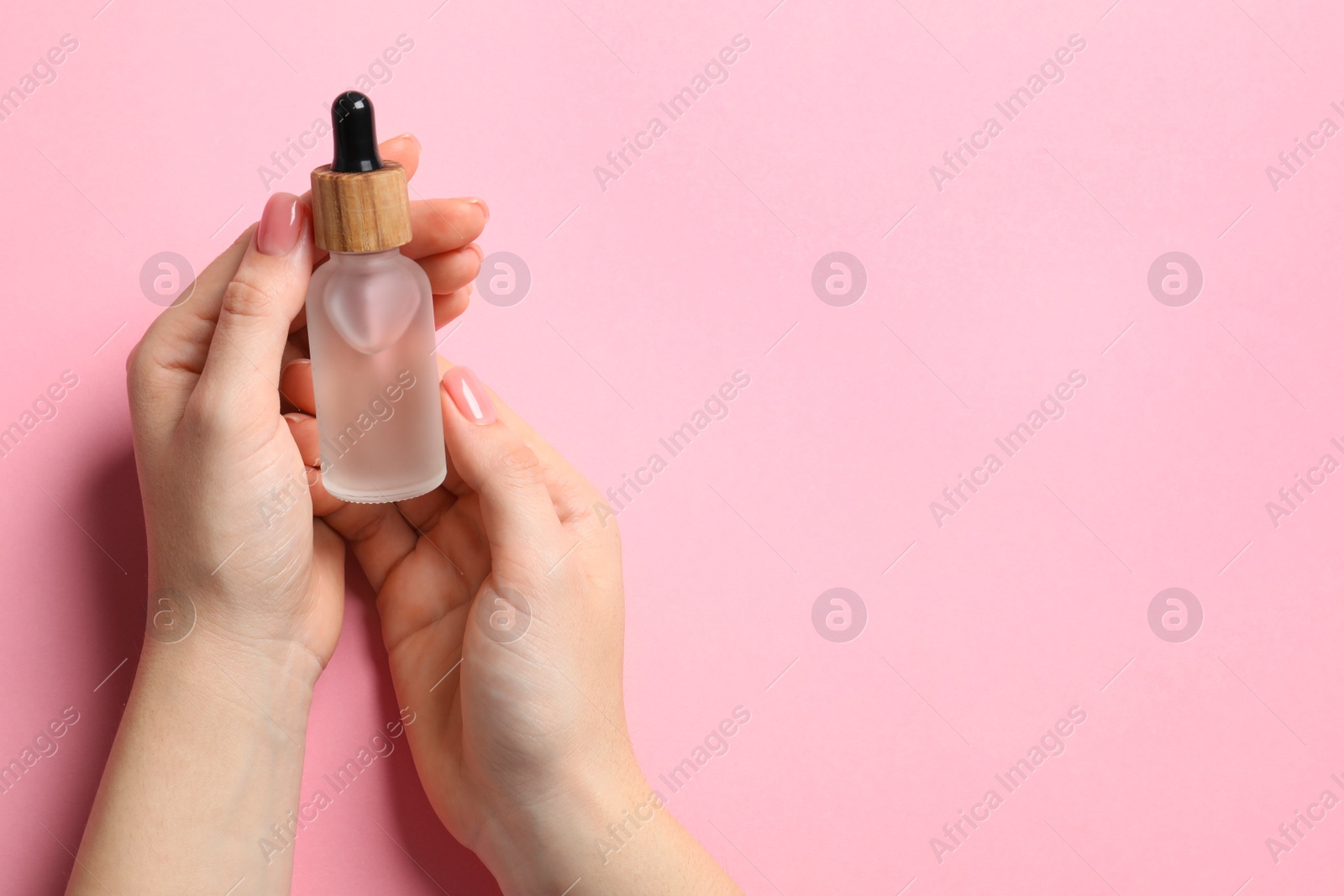 Photo of Woman holding bottle with serum on pink background, top view. Space for text