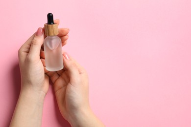 Woman holding bottle with serum on pink background, top view. Space for text