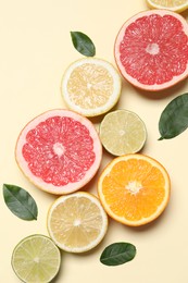 Different cut citrus fruits and leaves on beige table, flat lay