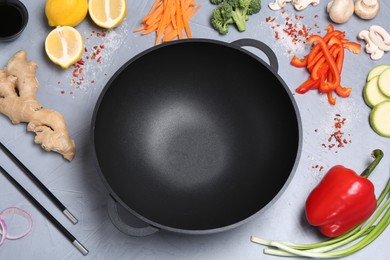 Wok, chopsticks and different products on grey table, above view