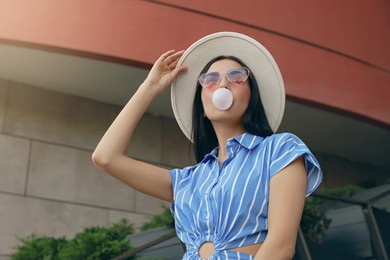 Stylish woman blowing gum near building outdoors