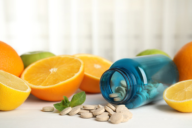 Bottle with vitamin pills and orange on white wooden table