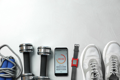 Smartphone with fitness app and sport accessories on white background, flat lay. Space for text