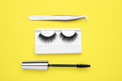 Photo of Fake eyelashes, mascara brush and tweezers on yellow background, flat lay