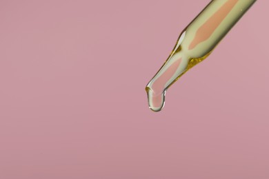 Photo of Dripping hydrophilic oil from pipette on pink background, closeup. Space for text