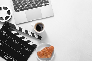 Photo of Movie clapper, film reel, laptop, coffee and croissant on light textured table, flat lay. Space for text