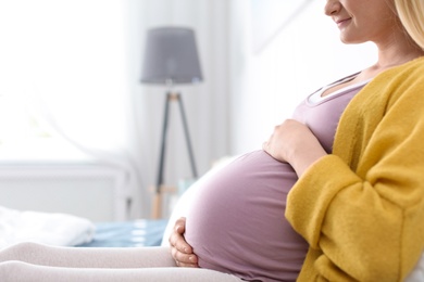 Photo of Pregnant woman resting on bed in light room, closeup. Space for text