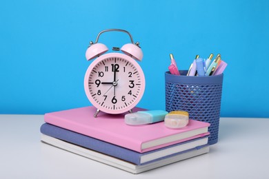 Photo of Different school stationery and alarm clock on white table against light blue background. Back to school