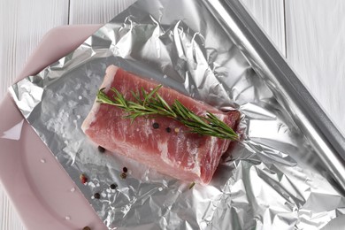 Photo of Aluminum foil with raw meat, rosemary and spices on white wooden table, top view
