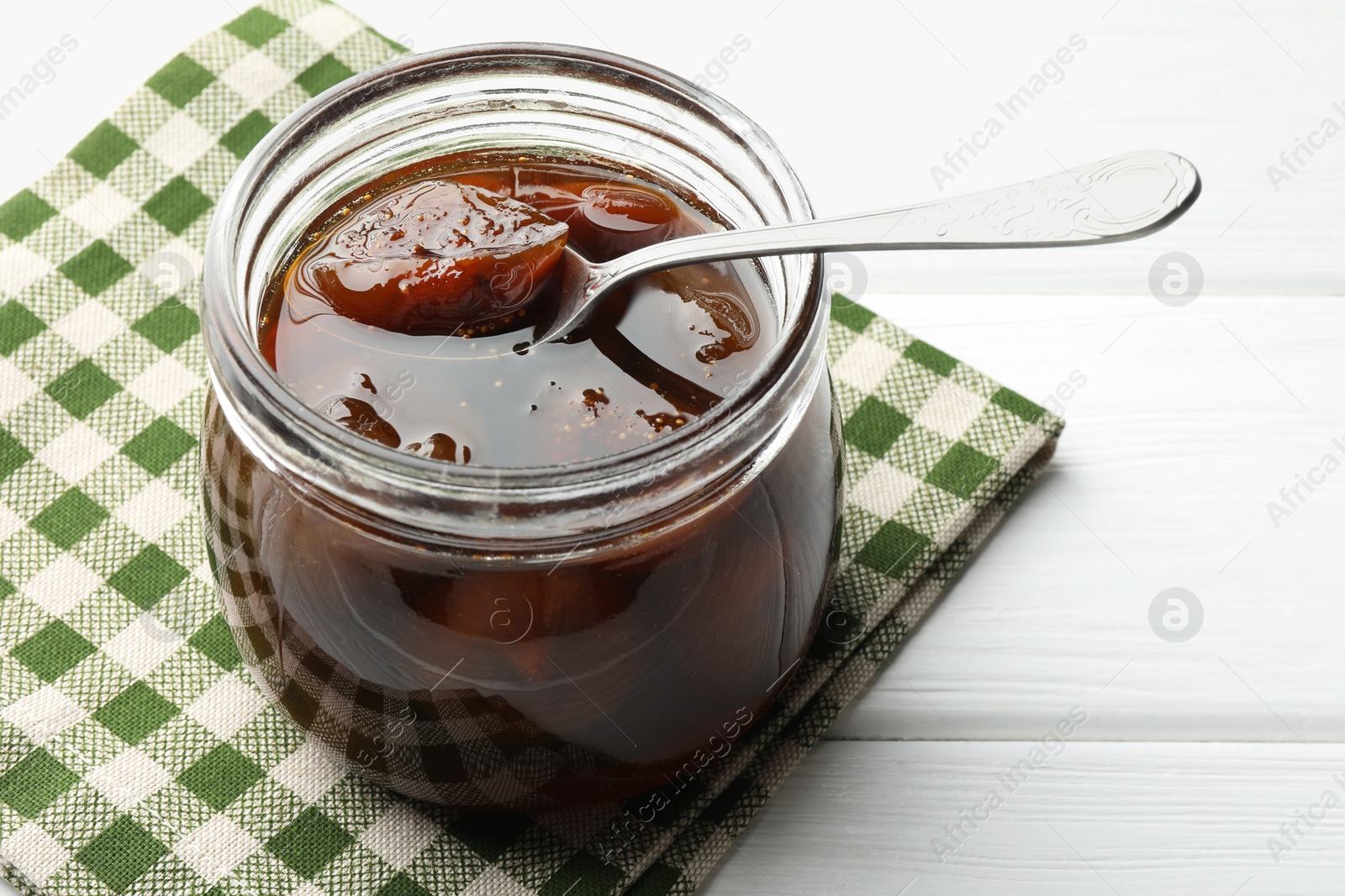 Photo of Jar of tasty sweet fig jam on white wooden table