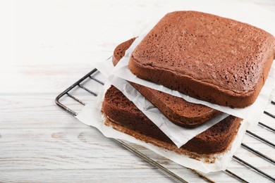 Photo of Layers of homemade chocolate sponge cake on white wooden table. Space for text