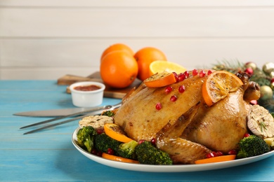 Photo of Delicious chicken with oranges, pomegranate and vegetables on light blue wooden table