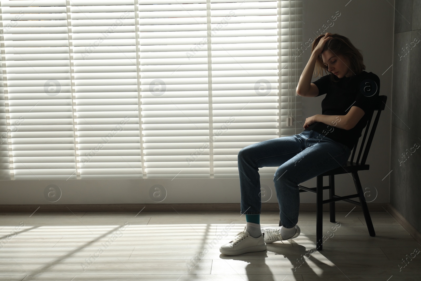 Photo of Sad young woman sitting on chair at home, space for text