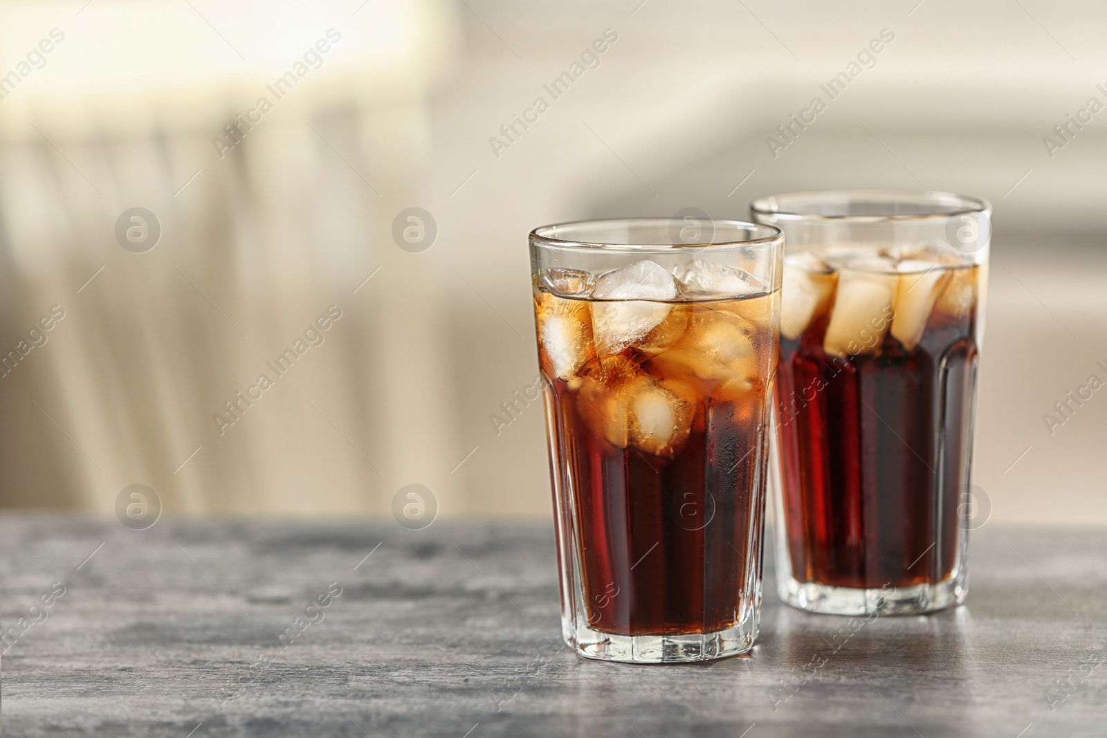 Photo of Glasses of cola with ice on table against blurred background, space for text