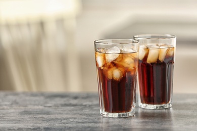 Glasses of cola with ice on table against blurred background, space for text