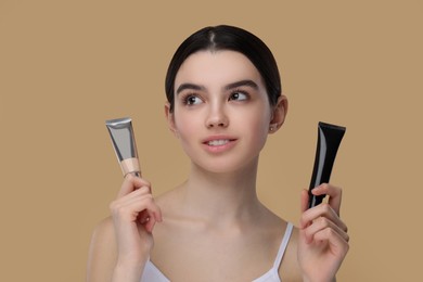 Teenage girl holding tubes with foundation on beige background