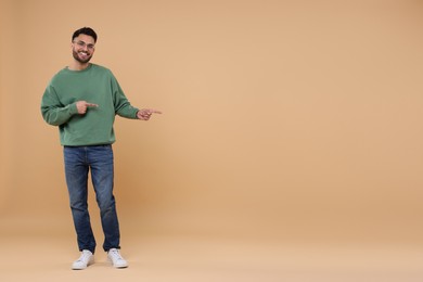 Happy young man pointing at something on beige background, space for text