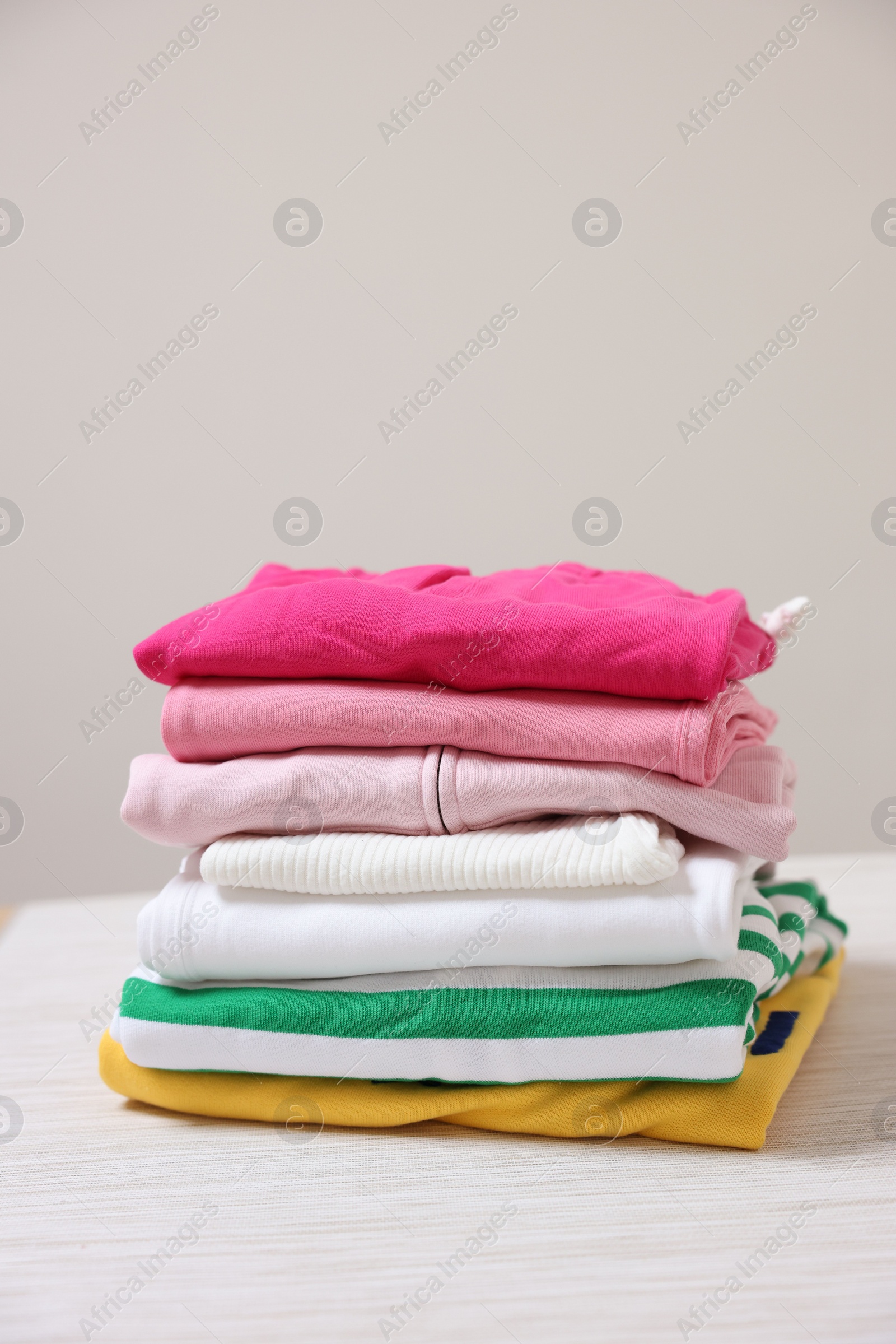Stack of folded clothes on table against beige background Photo of Stack of folded clothes on table against beige background