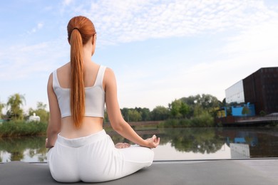 Woman practicing Padmasana on yoga mat outdoors, back view, space for text. Lotus pose