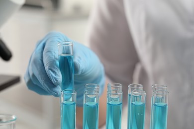 Photo of Scientist taking test tube with light blue liquid in laboratory, closeup