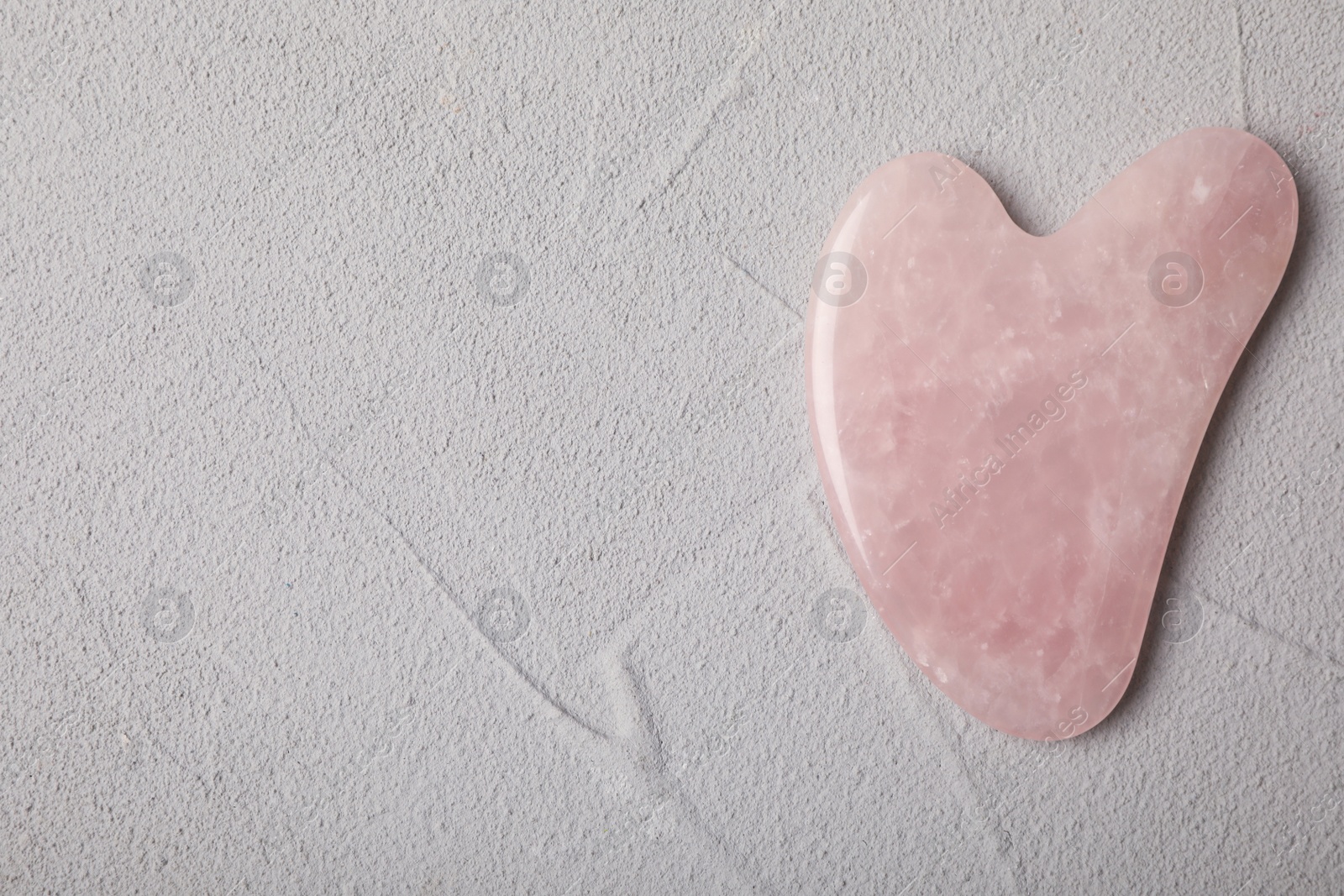 Photo of Rose quartz gua sha tool on grey table, top view. Space for text