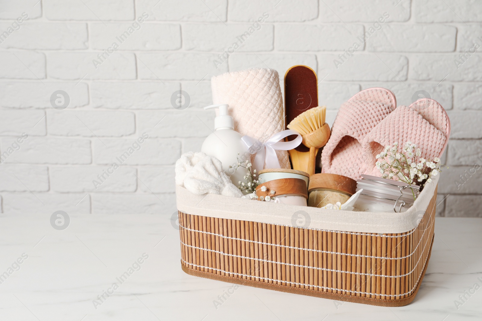 Photo of Spa gift set in wicker basket on white marble table. Space for text